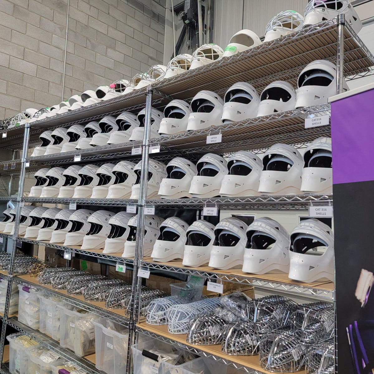 Rows of white LGR pro goalie mask shells and stainless steel cages on workshop shelves.